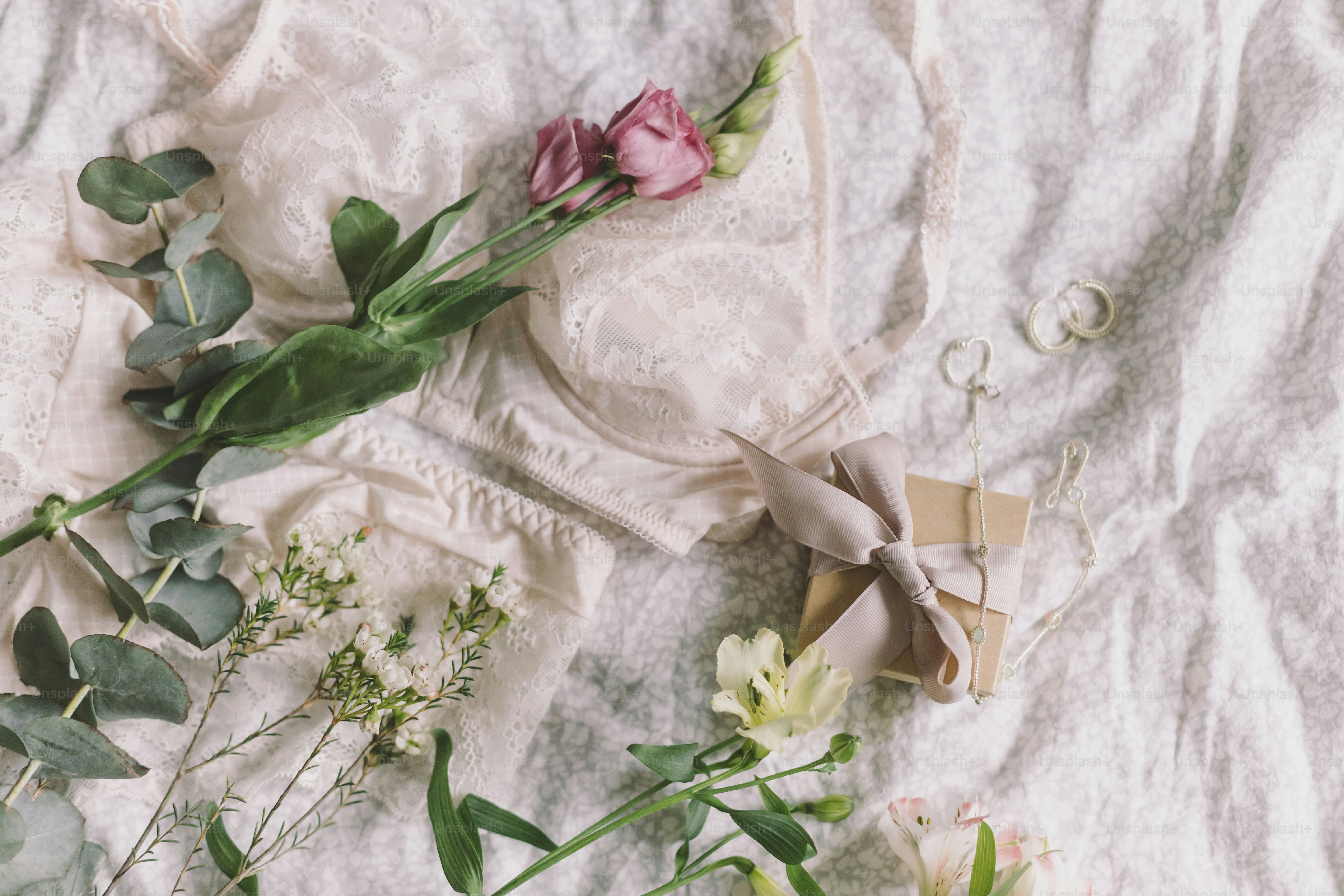 Stylish lace lingerie, gift box, modern jewelry and spring bouquet  on bed. Soft tender feminine image, sensual mood at home concept. Happy Women's day, woman essentials
