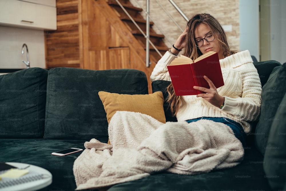 Shot of a young woman reading a book while relaxing on the sofa at home