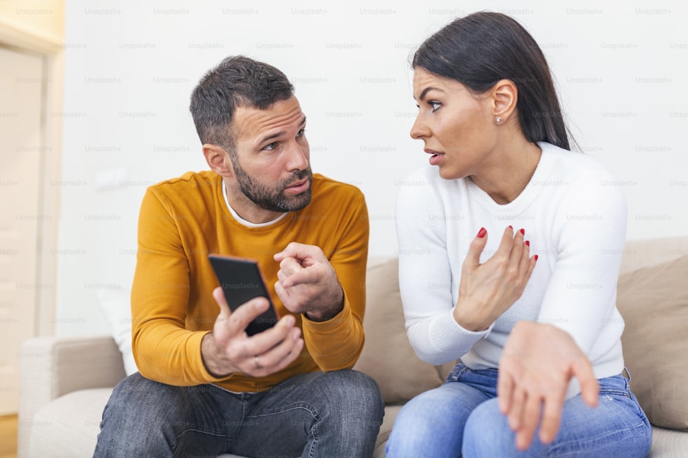 Boyfriend asking for an explanation to his cheater sad girlfriend sitting on a couch in the living room in a house interior