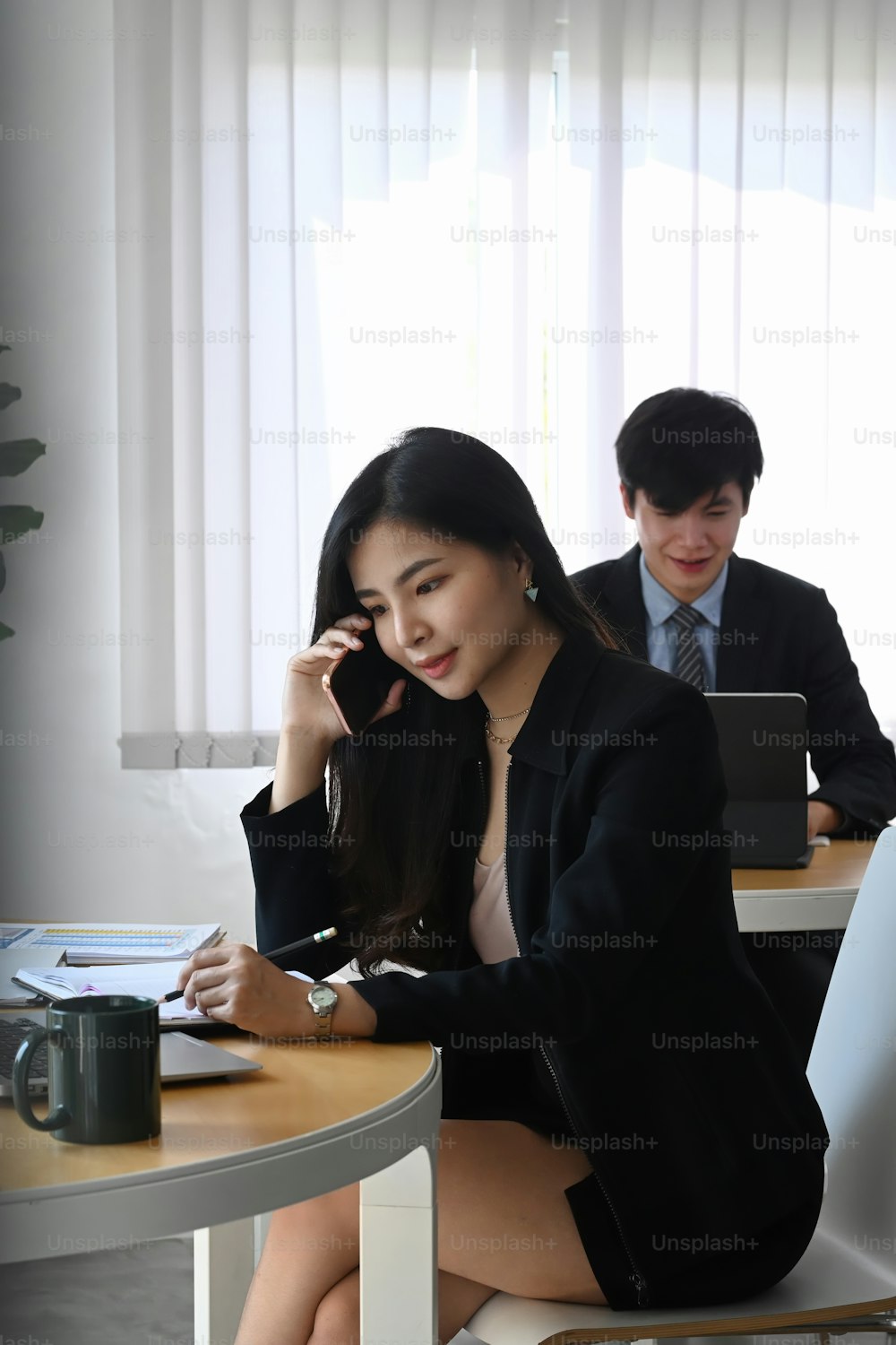 Retrato de empresária atraente falando no telefone celular e sentada no escritório.