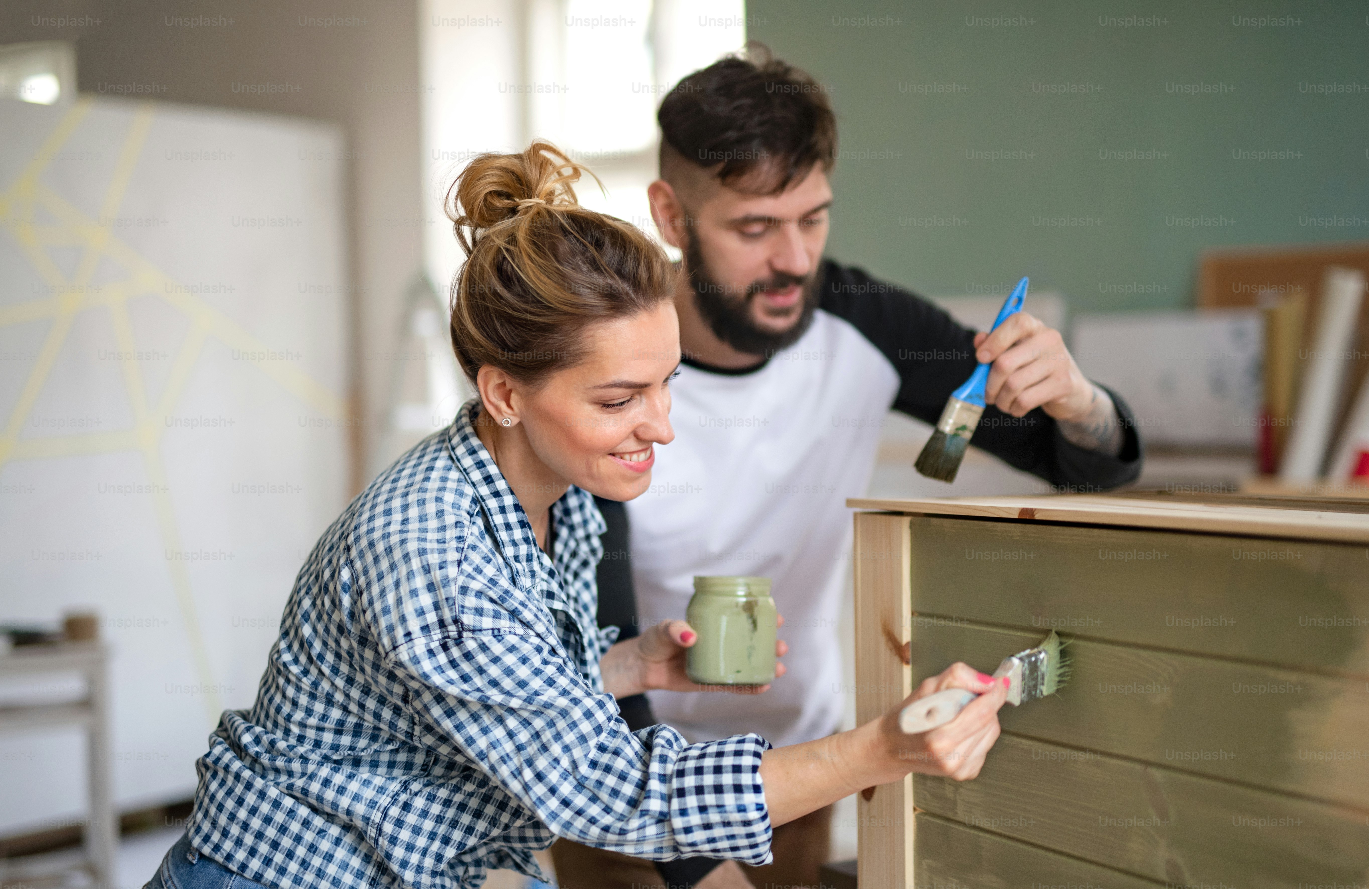 Bahagia pasangan dewasa pertengahan melukis furnitur di dalam ruangan di rumah, relokasi dan konsep diy.
