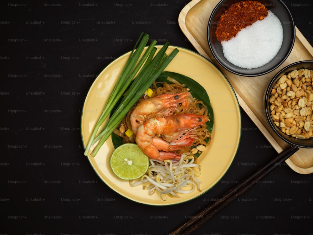 Vue de dessus de nouilles thaïlandaises sautées aux crevettes servies avec du citron vert, des germes de soja et de la ciboulette, pad thaï, cuisine thaïlandaise