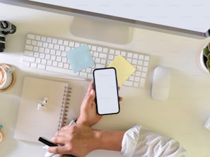 Overhead-Aufnahme eines Geschäftsmannes mit einem Smartphone in der Hand, während er am Computertisch arbeitet