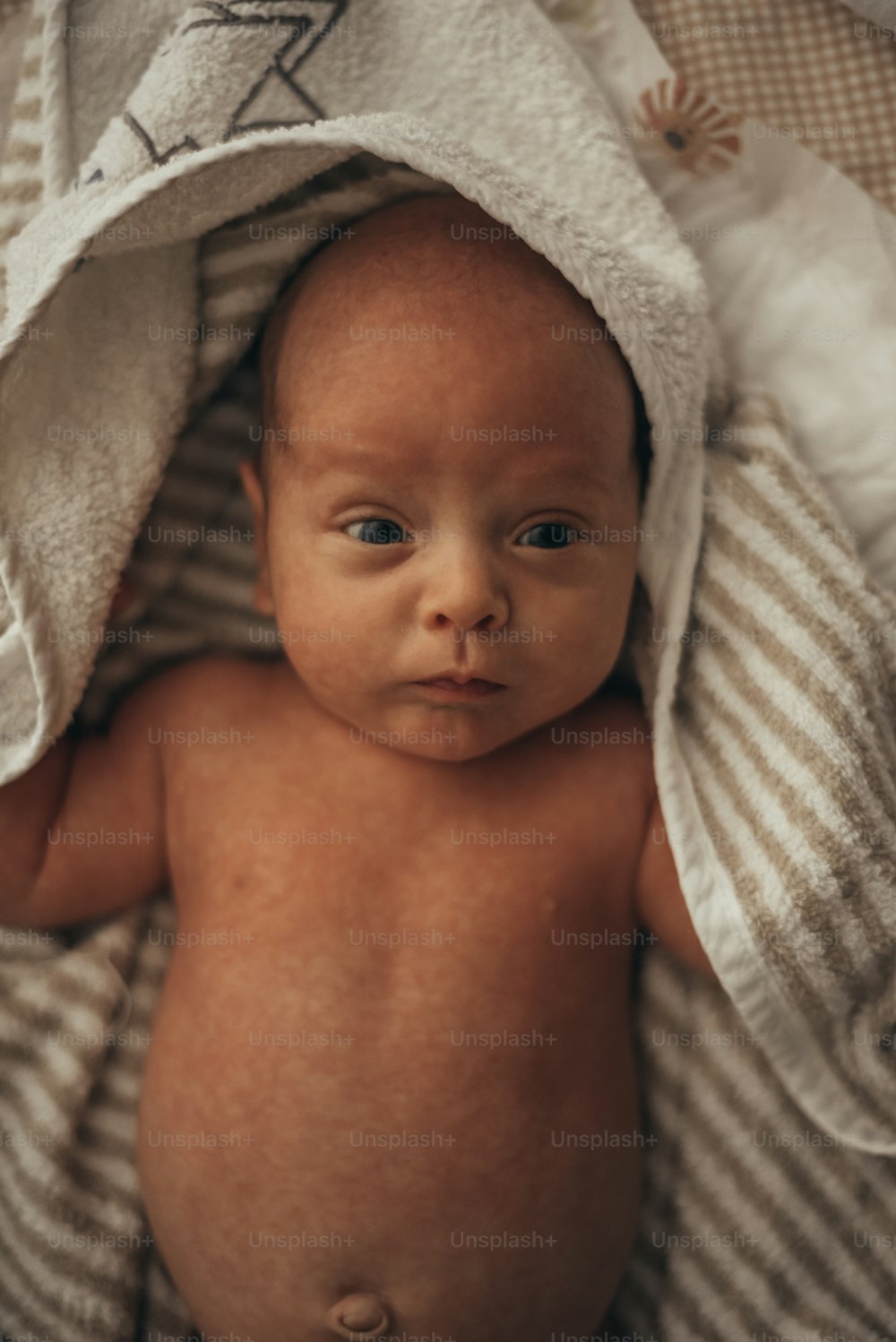 Foto de un adorable bebé envuelto en una toalla mientras está acostado en una cama después del baño en casa