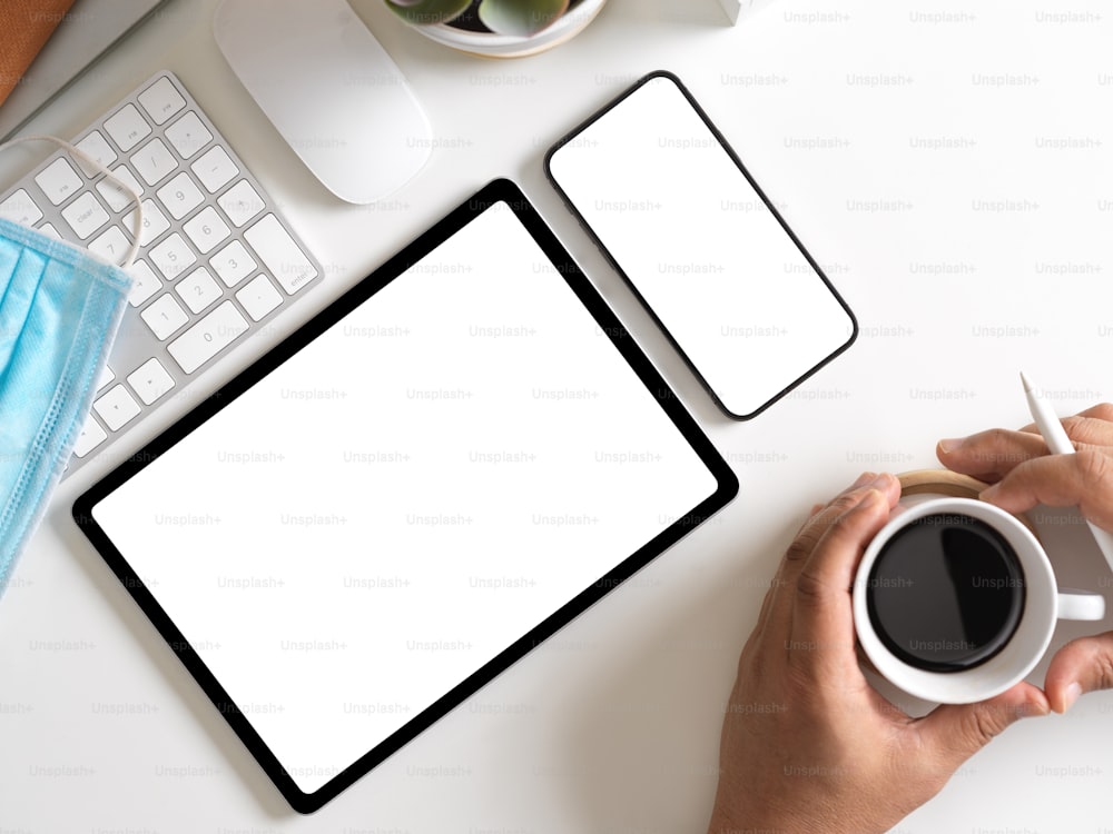 Vista dall'alto del maschio che tiene la tazza di caffè nelle sue mani sullo spazio di lavoro con tablet digitale, smartphone e forniture, percorso di ritaglio