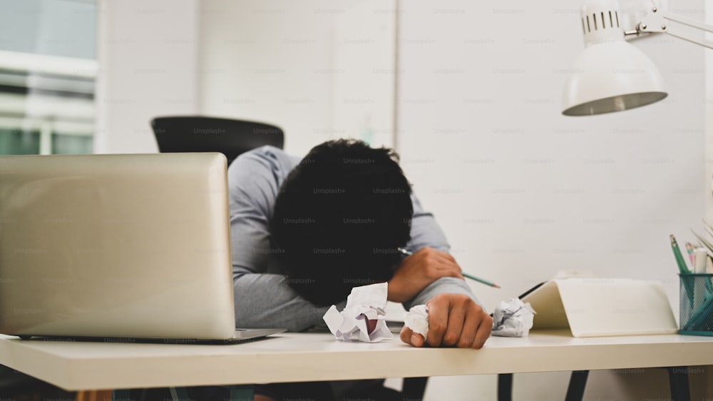 働き過ぎのビジネスマンは、オフィスの疲れで眠りに落ち、しわくちゃの紙のボールを持っていました。