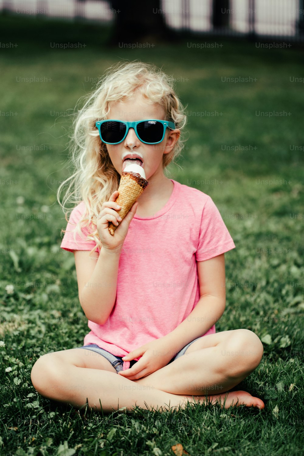 汚れた鼻と口ひげを生やしたサングラスのかわいくて面白い愛らしい女の子が、ワッフルコーンのアイスクリームを食べています。屋外でおいしい甘い冷たい夏の季節の食べ物を食べる幸せでクールなヒップスターの子供。夏の楽しみ。