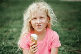 Menina adorável engraçada e fofa com nariz sujo e bigodes de leite comendo sorvete lambendo de cone de waffle. Criança comendo saborosa comida doce e fria de verão ao ar livre. Lanche de refeição congelada de verão.