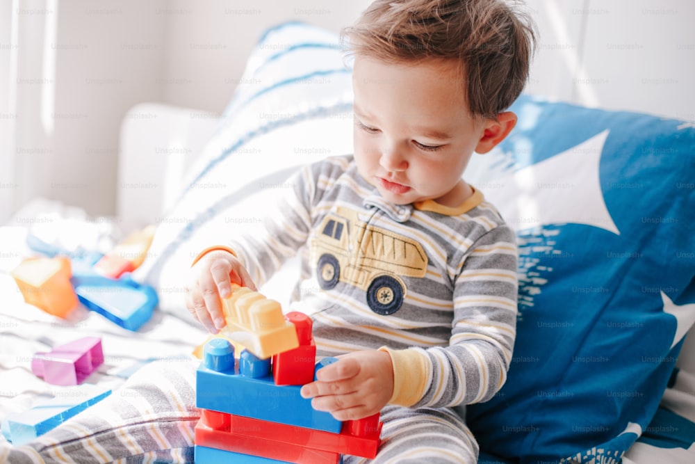 Cute baby toddler playing building with learning toy stacking blocks at home. Early age education. Kids hand brain and fine motor skills development. Logic activity for preschooler.