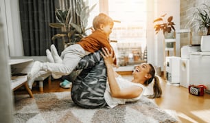 Schöne junge Mutter, die zusammen mit ihrem entzückenden kleinen Sohn Fitnesstraining und Yoga praktiziert. Sie genießen, spielen und lächeln.