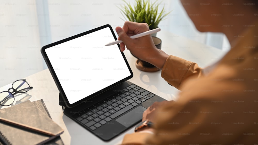 Vista de cerca del diseñador gráfico del joven que sostiene el lápiz óptico apuntando en la pantalla de la tableta digital en la oficina en casa.