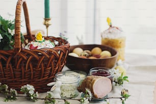 Traditional Easter food for blessing, homemade Easter bread, stylish easter eggs and blooming spring flowers on linen napkin on rustic table. Happy Easter! Festive breakfast