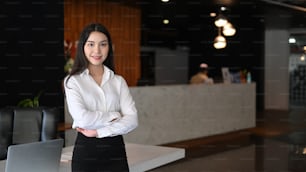Confident businesswoman standing with crossed arms in modern office room.