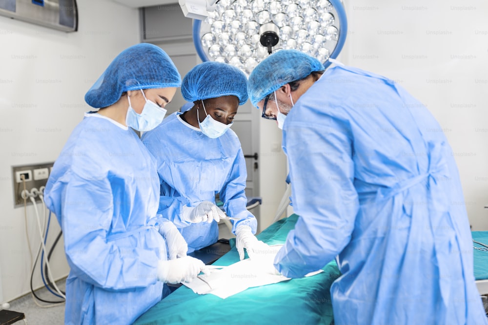 Portrait d’une équipe de chirurgiens multiethniques au travail dans une salle d’opération. Plusieurs médecins entourent le patient sur la table d’opération pendant leur travail. Équipe de chirurgiens au travail dans la salle d’opération.