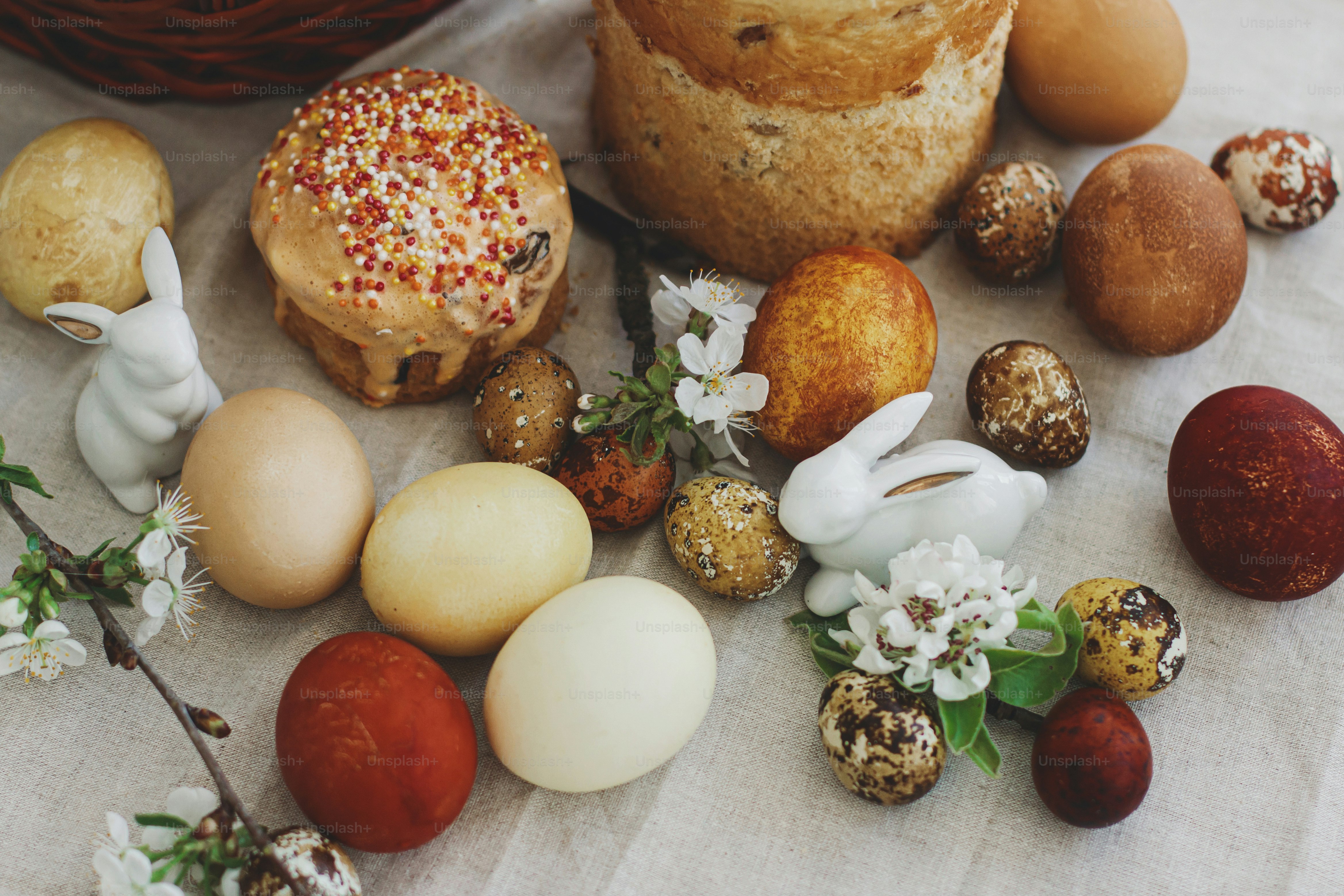 Modern easter eggs, Easter bread, wicker basket, bunny and blooming spring flowers on rustic