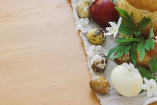 Stilvolle Ostereier, blühende Frühlingsblumen und selbstgebackenes Osterbrot auf rustikaler Tischplatte. Frohe Ostern! Platz für Text. Moderne natürlich gefärbte Eier und traditionelles Osteressen