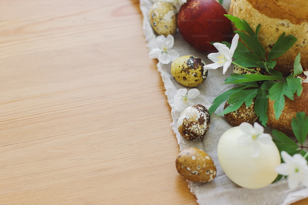 세련된 부활절 달걀, 피는 봄 꽃, 소박한 테이블에 수제 부활절 빵. 행복한 부활절! 텍스트를 위한 공간입니다. 현대 자연 염색 계란과 전통 부활절 음식