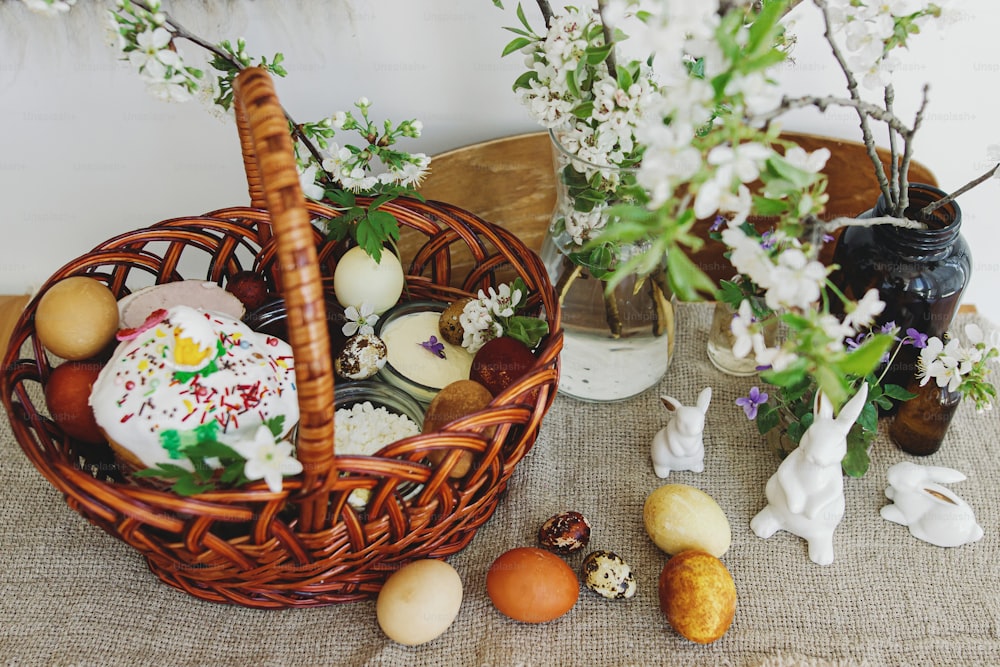 Stilvolle Ostereier, hausgemachtes Osterbrot, leckeres traditionelles Osteressen im Weidenkorb und blühende Frühlingsblumen auf Leinenserviette auf rustikalem Tisch. Frohe Ostern! Festliches Frühstück