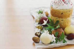 ¡Felices Pascuas! Elegantes huevos de Pascua, flores de primavera en flor y pan de Pascua casero en una mesa rústica.  Espacio para el texto. Huevos teñidos naturales modernos y comida tradicional de Pascua