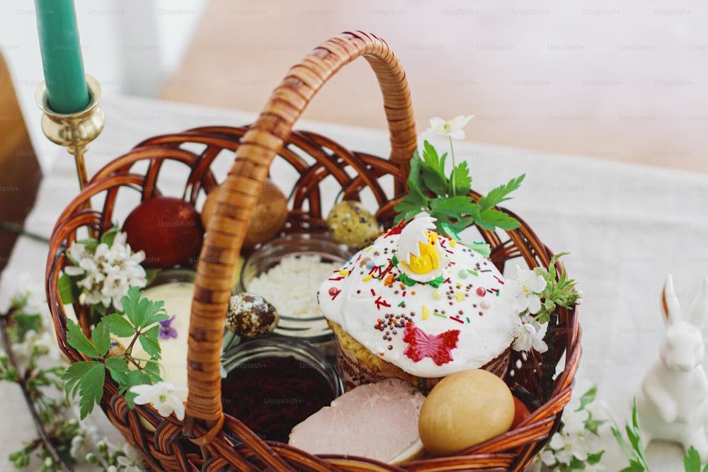 Delicious Easter food, stylish easter eggs, beets, cheese, butter, ham, homemade Easter bread in wicker basket with blooming spring flowers on rustic table, orthodox traditions. Happy Easter!