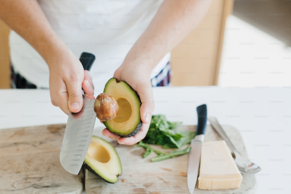 Young man peeling avocado and making healthy toasts in modern white kitchen. Perfectly ripe avocado in hands. Healthy eating and Home cooking concept