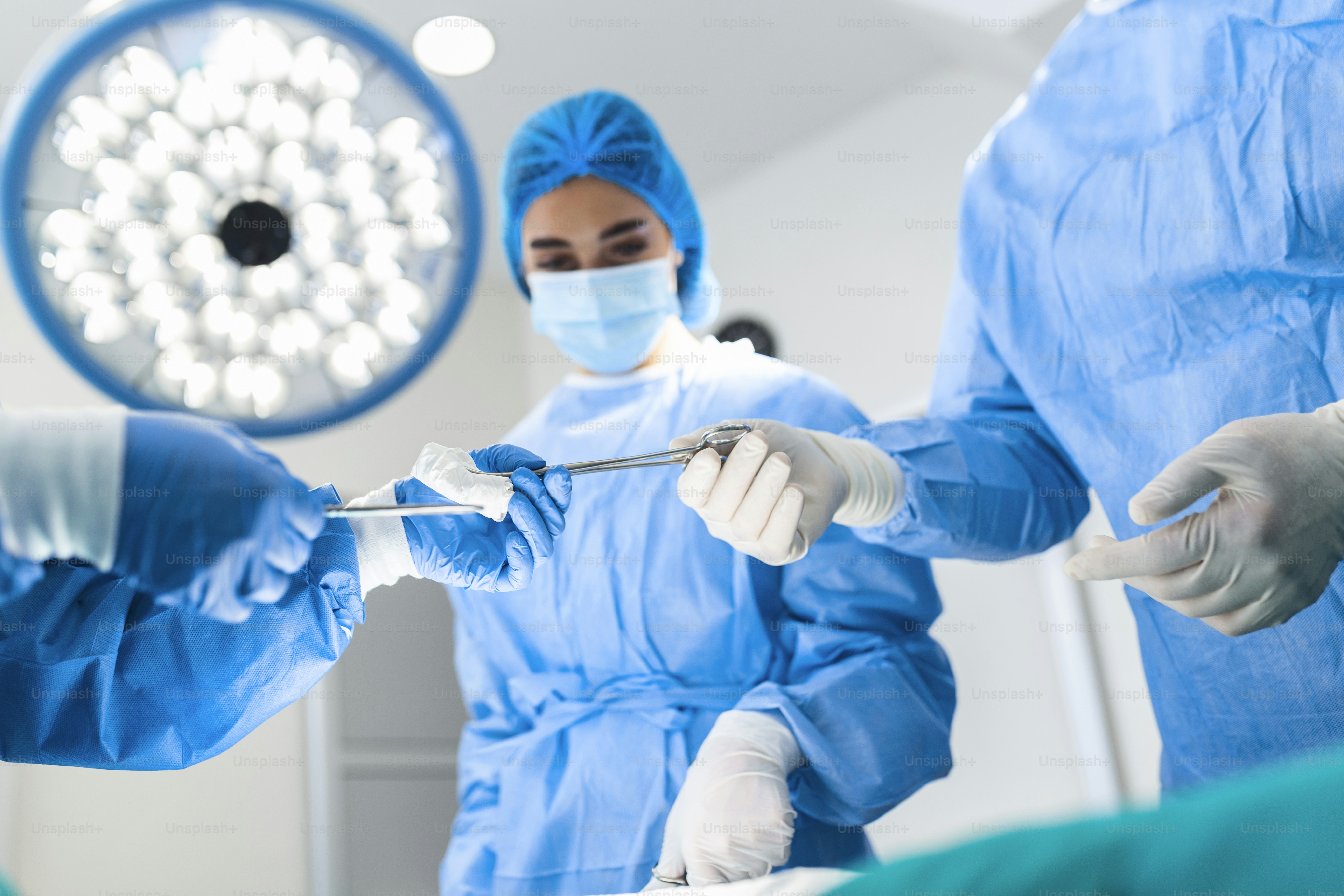 Medical Team Performing Surgical Operation in Bright Modern Operating Room. Group of surgeons at work in operating theater toned in blue. Medical team performing operation