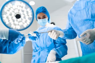 Medical Team Performing Surgical Operation in Bright Modern Operating Room. Group of surgeons at work in operating theater toned in blue. Medical team performing operation