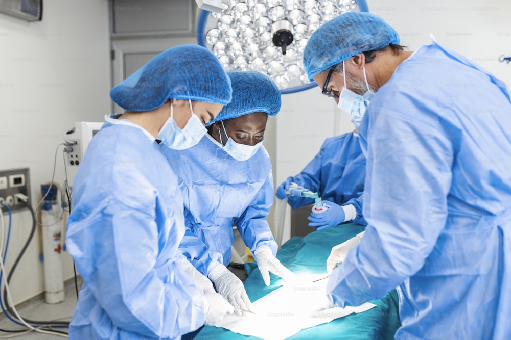수술을 수행하는 의료진. 수술실에서 일하는 외과 의사 그룹이 파란색으로 톤을 띠고 있습니다. 보험 광고를 위한 병원 수술실에서 의사 수술 개념.