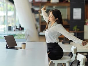 Portrait of businesswoman relaxing in office room, stretching her arms and back while sitting at workplace