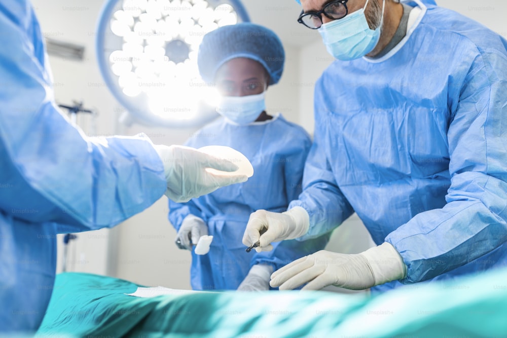 Surgeon and his assistant performing cosmetic surgery in hospital operating room. Surgeon in mask during medical procadure. Breast augmentation, enlargement, enhancement