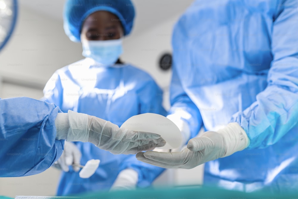 Cirurgião e seu assistente realizando cirurgia plástica em centro cirúrgico hospitalar. cirurgia de aumento de mama na sala de cirurgia cirurgião ferramentas implante.