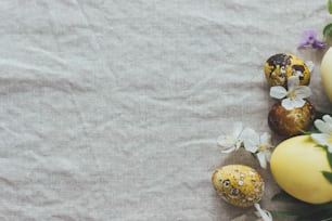 Ovos de Páscoa com flores da primavera sobre fundo de linho rústico, postura plana com espaço para texto. Elegantes ovos modernos de páscoa e codorna com corante natural e flores de primavera. Cartão de felicitações das estações estéticas
