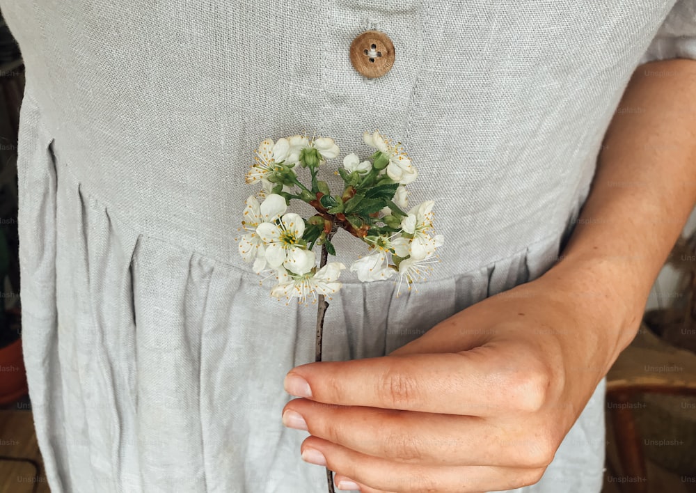 Woman in rustic linen dress holding blooming cherry  branches. Hello spring and Happy Easter! Aesthetic simple image. Spring flowers in hands