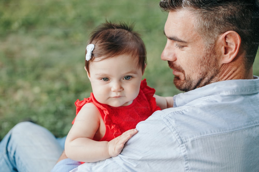 Middle age Caucasian proud father holding baby daughter. Family dad and daughter sitting together outdoor in park on summer day. Life with kids children. Happy lifestyle family of two.