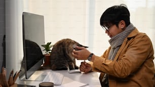 自宅で仕事をし、かわいい猫と遊�んでいる若い男性の横から見た写真。
