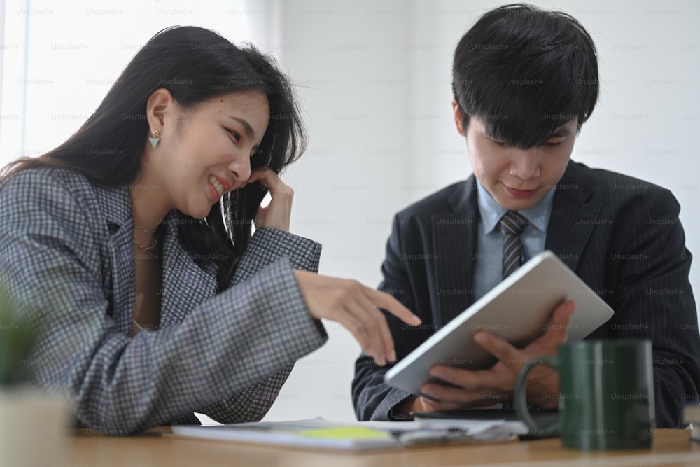 Dois felizes parceiros de negócios usando tablet digital e trabalhando juntos no escritório.