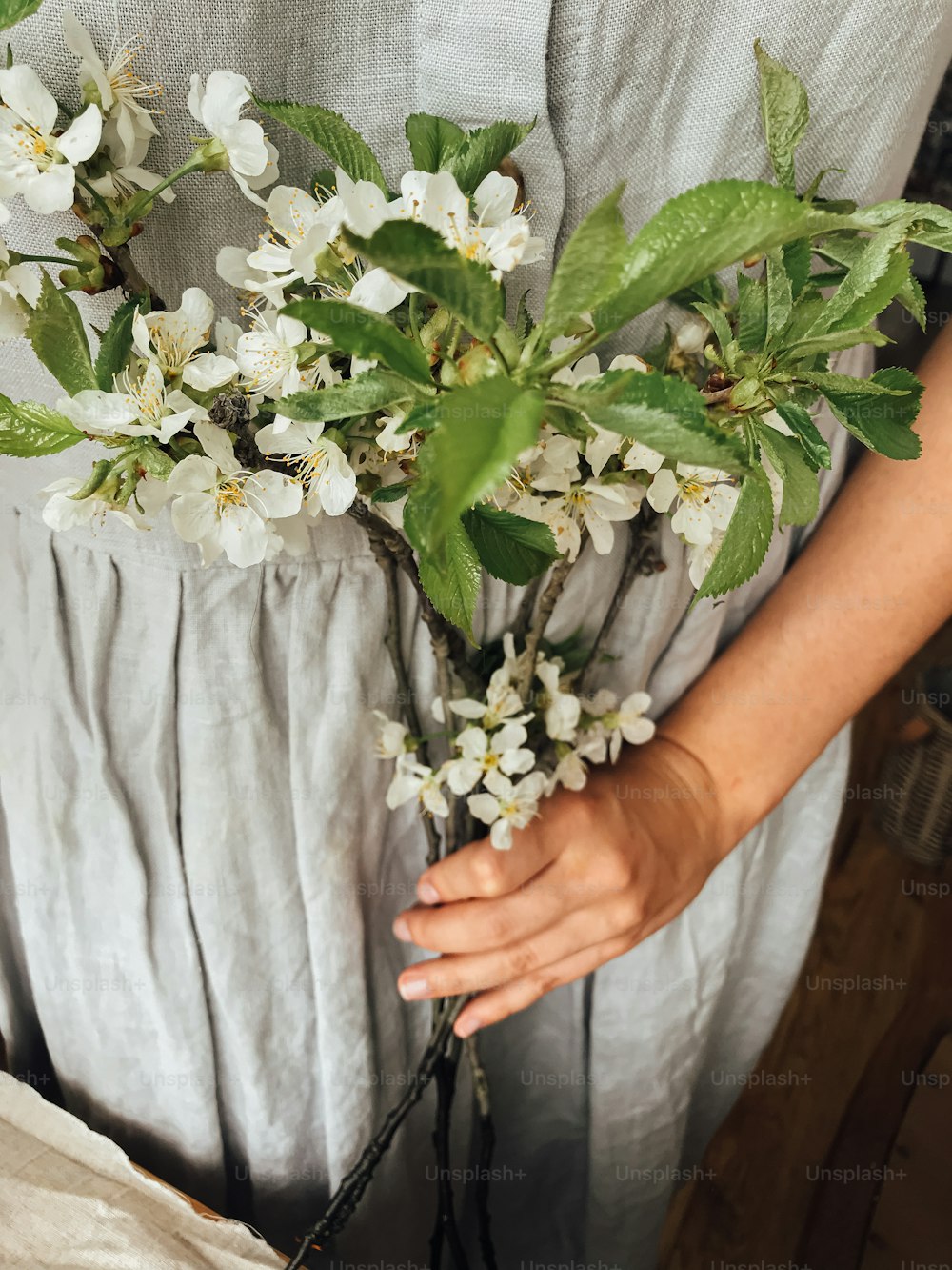 Woman in rustic linen dress holding blooming cherry and apple branches. Hello spring and Happy Easter! Aesthetic simple image. Spring flowers in hands