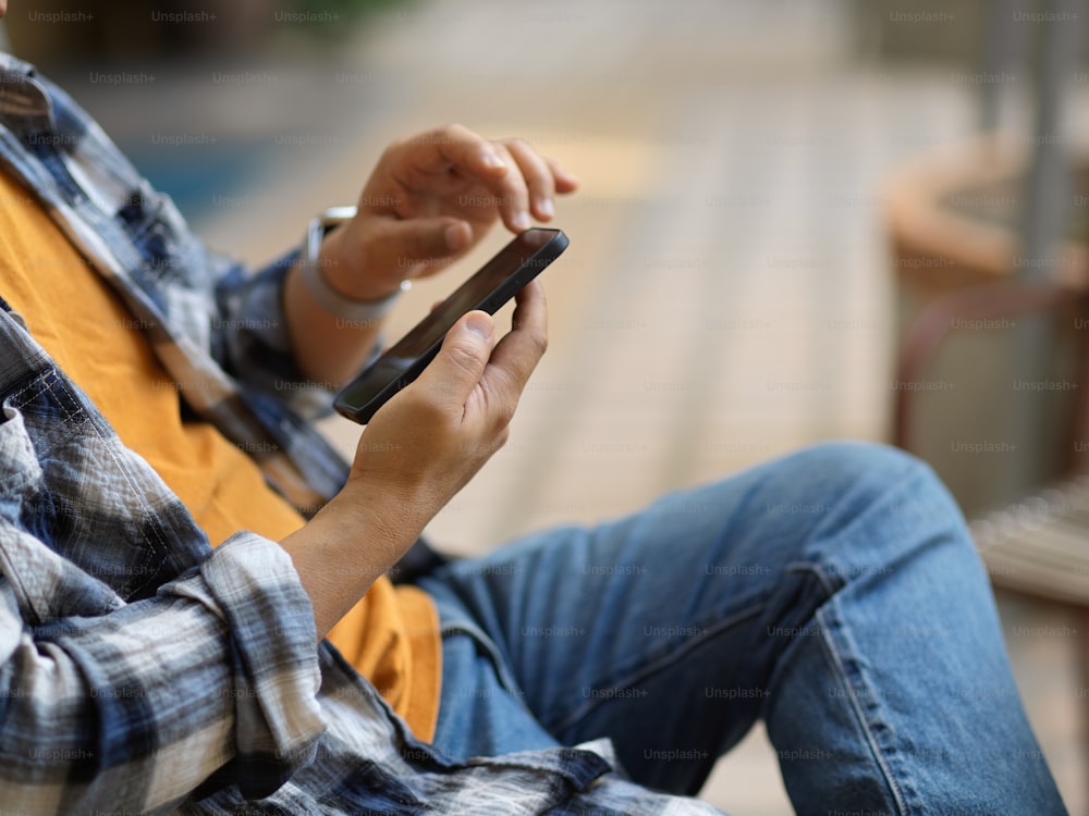 Side view of male freelancer using smartphone on his hands while relaxed sitting in blurred background