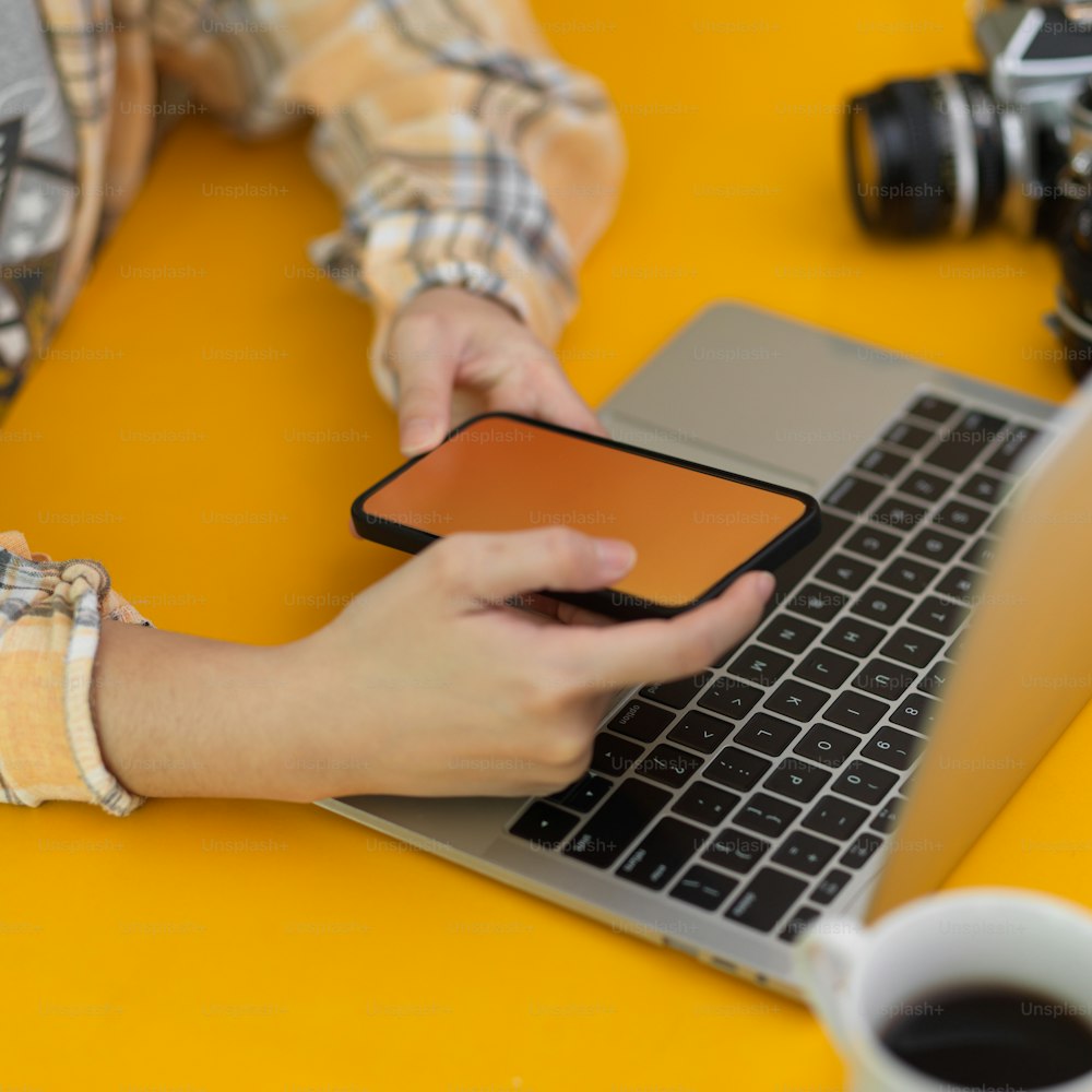 Geschnittene Aufnahme einer Fotografin, die Smartphone und Laptop auf einem stilvollen Arbeitsplatz im Home-Office-Raum arbeitet