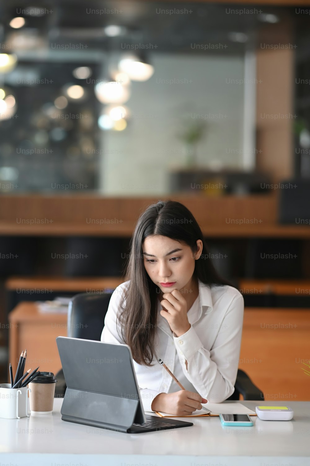 Retrato da empresária atraente olhando na tela do computador tablet enquanto está sentada em seu local de trabalho.