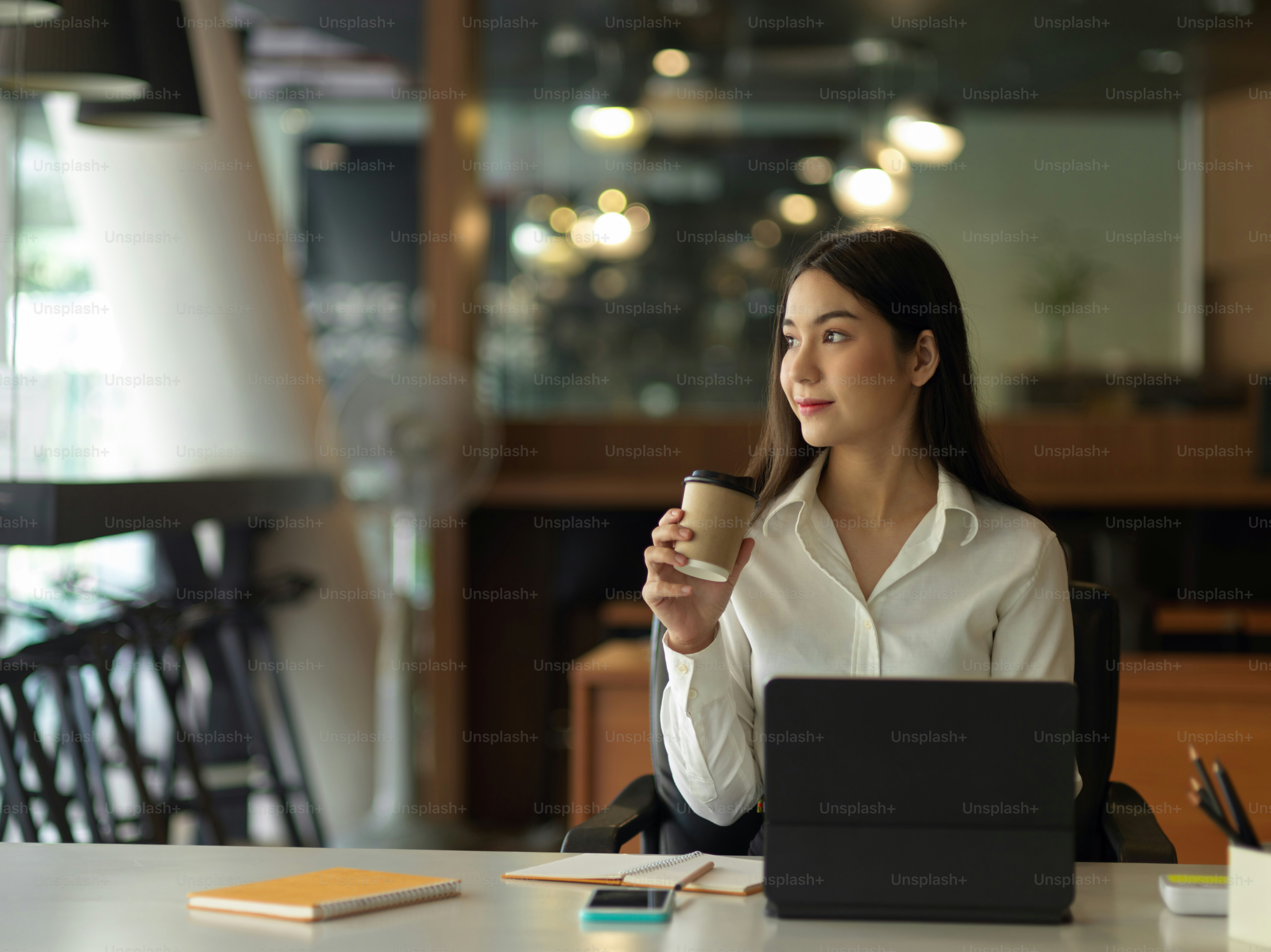 コーヒーを飲みながらリラックスし、オフィスの窓から外を眺める女性サラリーマンのポートレート