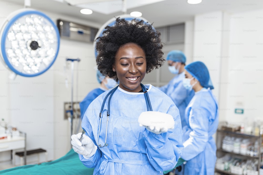 수술실 내부에서 실리콘 유방 보형물을 들고 있는 아프리카계 미국인 성형외과 의사. 성형 수술 개념