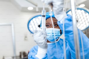 手術室で薬を点滴に通すアフリカ系アメリカ人の女性医師 - 手術の概念