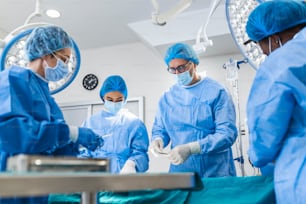 Multiethnisches Gesundheitspersonal führt Operationen am Patienten im Operationssaal durch. Ärztliche Kollegen, die in der Notaufnahme des Krankenhauses operieren. Sie sind in Peelings