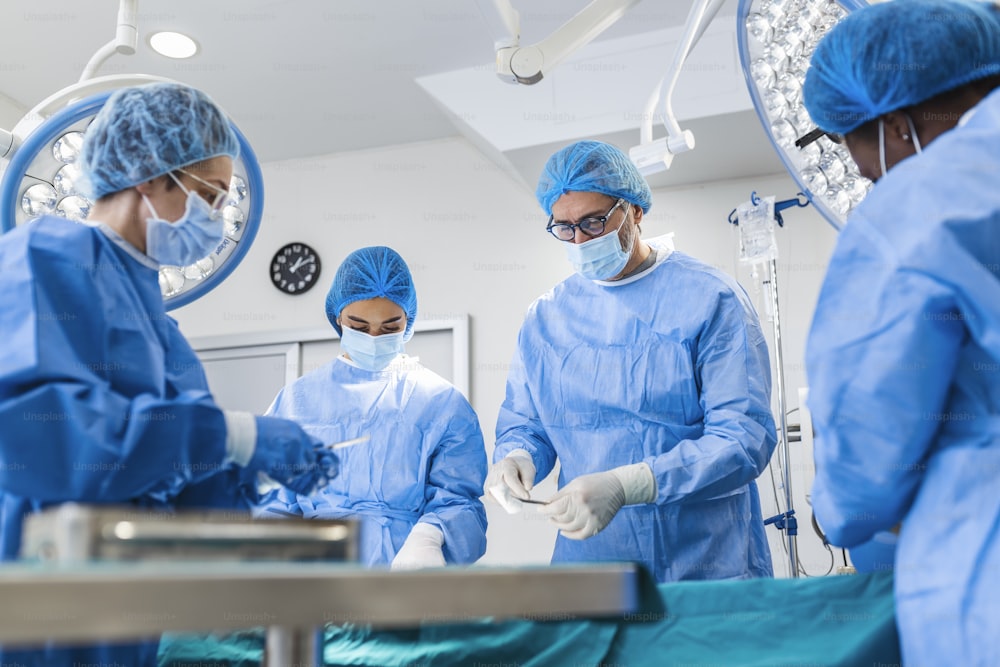 Multiethnisches Gesundheitspersonal führt Operationen am Patienten im Operationssaal durch. Ärztliche Kollegen, die in der Notaufnahme des Krankenhauses operieren. Sie sind in Peelings