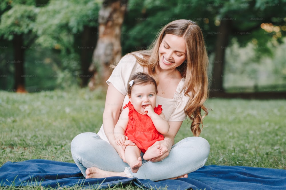 Mothers Day holiday. Young smiling Caucasian mother and girl toddler daughter hugging in park. Mom embracing child baby on summer day outdoor. Happy authentic family childhood lifestyle.