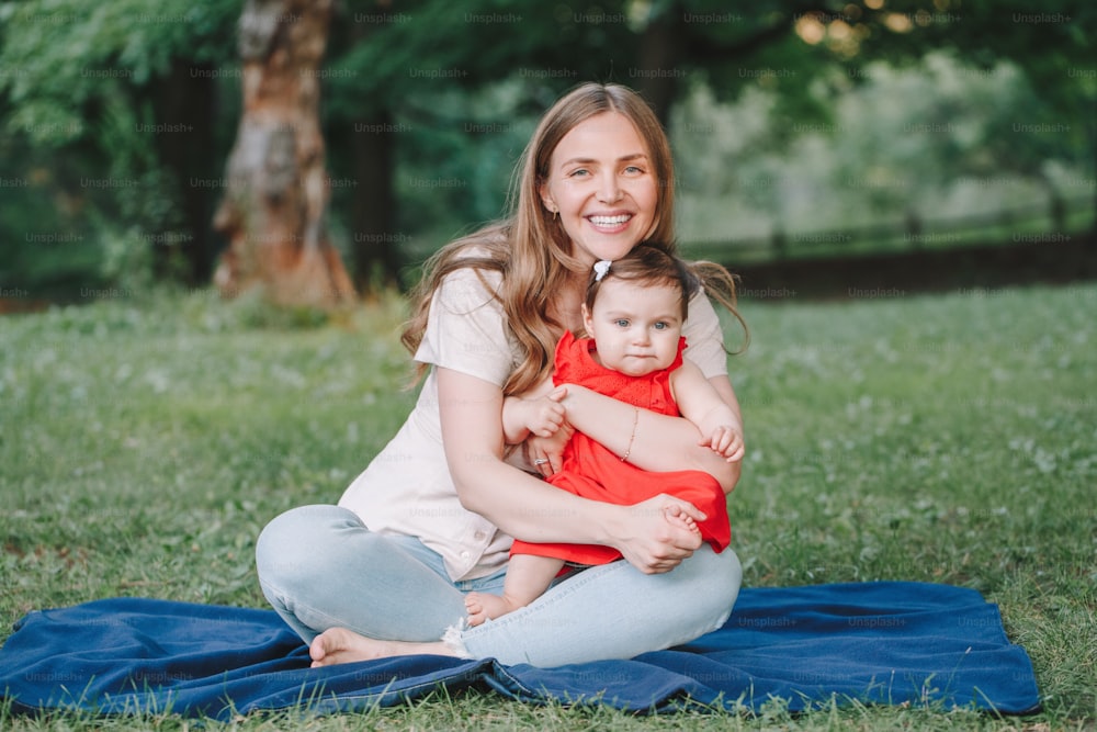 Mothers Day holiday. Young smiling Caucasian mother and girl toddler daughter hugging in park. Mom embracing child baby on summer day outdoor. Happy authentic family childhood lifestyle.