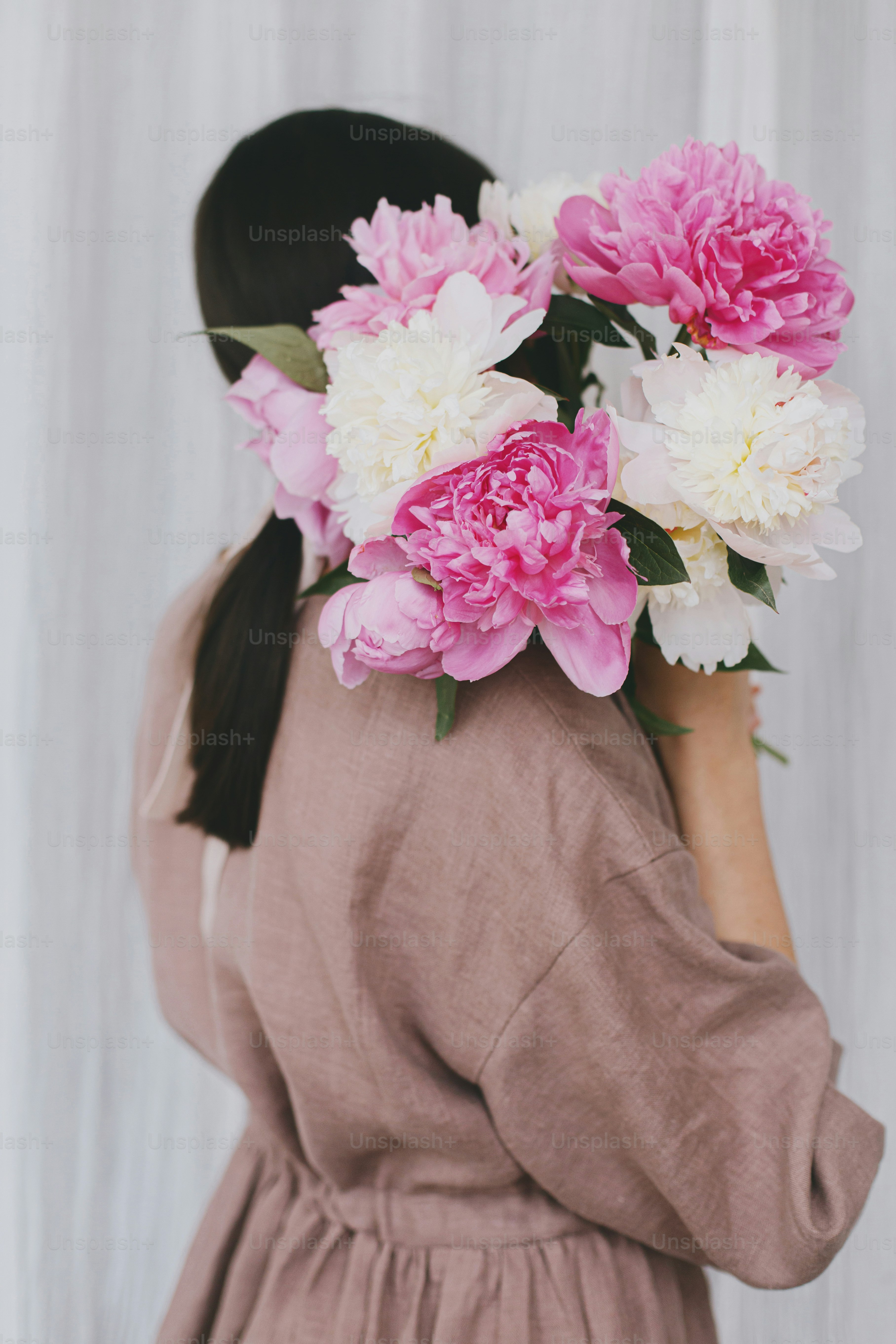Stylish woman in linen dress holding peony bouquet on background of ...