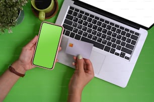 Overhead view of woman holding credit card and smart phone on green background.