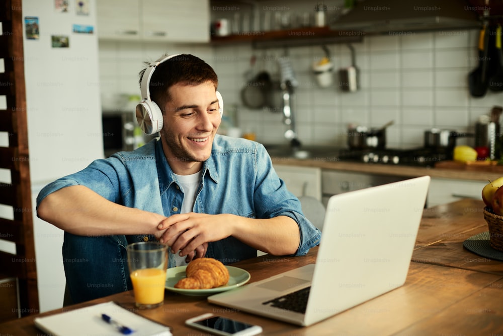 Homem feliz usando fones de ouvido enquanto navega na rede em um computador em casa.